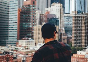 A man in casual attire observing the iconic New York City skyline from a bridge.